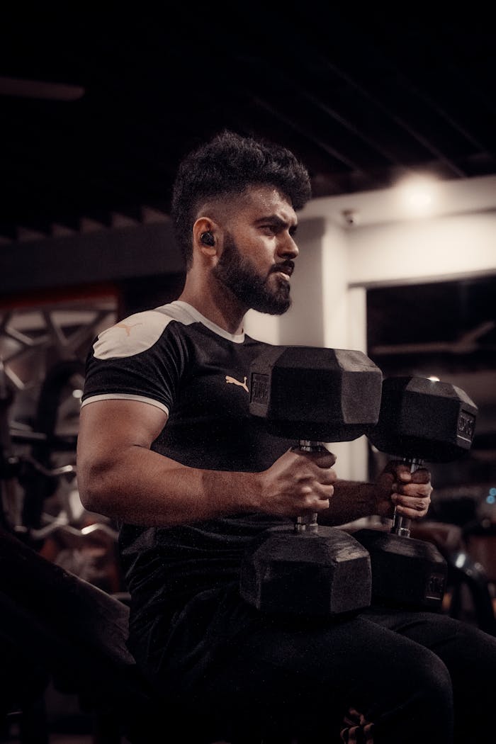 Man engaged in a focused dumbbell workout in a gym setting, emphasizing strength and dedication.